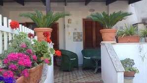 Un espacio al aire libre cubierto con plantas en macetas, una silla verde y una mesita.
