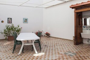 A room with a tiled floor, a white table with chairs, a potted plant, and a wooden door leading to a bathroom. - VILLETTA AL MARE OTRANTO (OTRANTO)