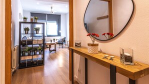 A hallway with a wooden console table, a round mirror, and a view into a living area with a dining table and chairs. - Nice apartment in Vila de Gracia (Barcelona)