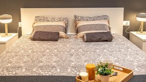 A neatly made bed with patterned bedding, two bedside lamps, and a tray with candles and a plant on the bedside table. - Nice apartment in Vila de Gracia (Barcelona)