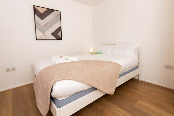 Un lit simple avec une tête de lit blanche, une couverture beige et un tableau abstrait accroché au mur.