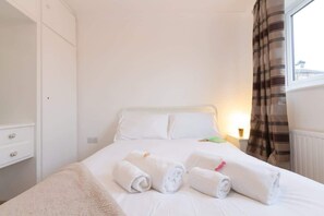 Une chambre d’hôtel avec un lit, des oreillers, une table de chevet, une lampe et une fenêtre avec des rideaux.