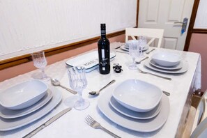 A dining table set with white plates, silverware, and a bottle of wine.