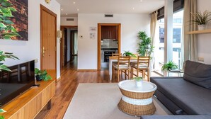 Ein modernes Wohnzimmer mit einer Couch, einem Couchtisch und einem Essbereich mit Stühlen. Im Hintergrund ist eine Küche zu sehen.