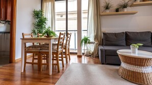 Ein modernes Wohnzimmer mit Essbereich, grauem Sofa, Holztisch und Topfpflanzen.