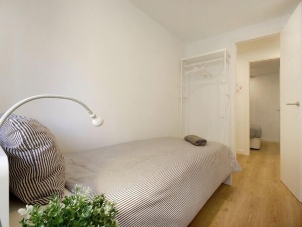 Un dormitorio pequeño y ordenado con una cama individual, una lámpara de noche, un cojín a rayas y una planta pequeña.