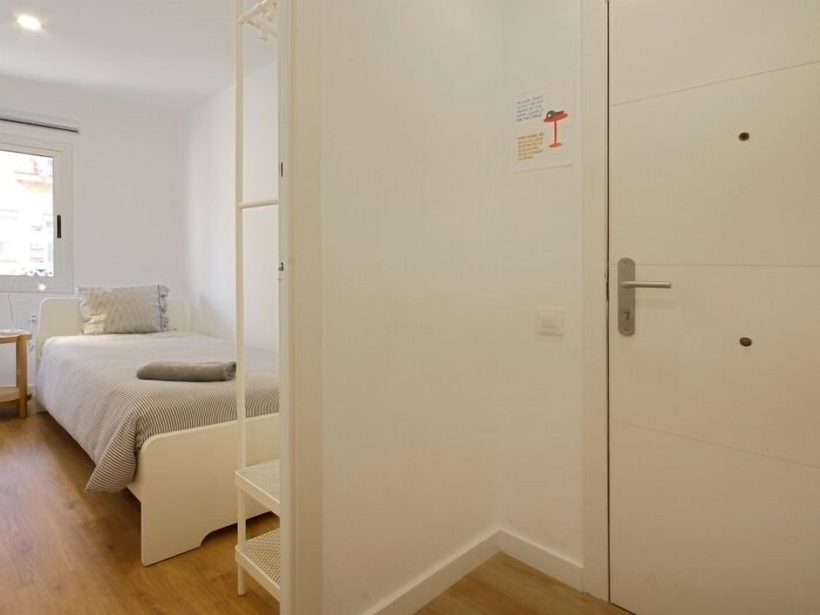 Un dormitorio con cama, una mesita y un armario blanco.