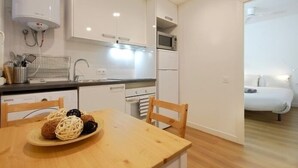 A compact kitchen with white cabinets, a microwave, and a dishwasher. There is a dining table with chairs and a plate of food. - Functional apartment near Barcelona (L'Hospitalet de Llobregat)