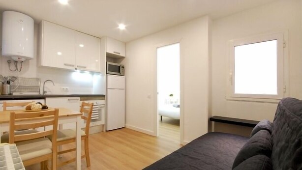 A compact living space with a kitchenette, a dining area, and a seating area with a couch. - Functional apartment near Barcelona (L'Hospitalet de Llobregat)