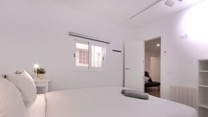 A minimalist bedroom with a large bed, a small bedside table, a window, and a wardrobe. - Functional apartment near Barcelona (L'Hospitalet de Llobregat)