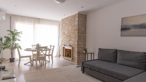 A modern living room with a grey sofa, a dining table with chairs, a fireplace, and a large window with sheer curtains. - Beautiful apartment in down town Barcelona (Barcelona)