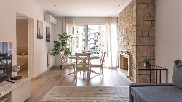 A modern living room with a dining area, a grey sofa, a fireplace, and a view of the cityscape. - Beautiful apartment in down town Barcelona (Barcelona)