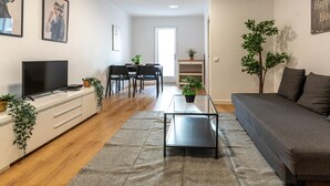 Ett modernt vardagsrum med en platt-TV, en soffa, ett soffbord och en matplats med stolar och ett bord.