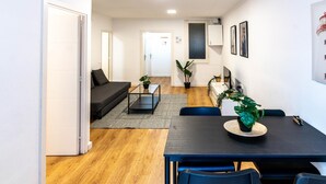 Ett modernt vardagsrum med en mörk soffa, ett soffbord i glas och en matplats med ett mörkt bord och blå stolar.