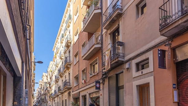A narrow street lined with multi-story buildings, some with balconies and shops on the ground floor.