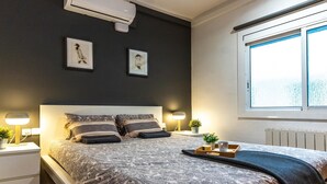 A modern bedroom with a large bed, bedside tables with lamps, a window with a view, and artwork on the wall.