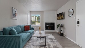 A modern living room with a teal sofa, a coffee table, a fireplace, and a TV mounted on the wall. - The Landry 157 | Spacious and Cozy 1 Bedroom 1bth (Arlington)