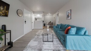A modern living room with a teal sofa, a coffee table, and a cityscape painting on the wall. - The Landry 157 | Spacious and Cozy 1 Bedroom 1bth (Arlington)