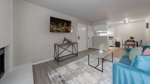 Un salon moderne avec un canapé bleu, une table basse et un tableau représentant un paysage urbain accroché au mur.