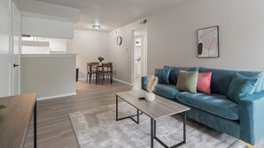 Un salon moderne avec un canapé de couleur turquoise, une table basse en bois et, au fond, un coin repas.