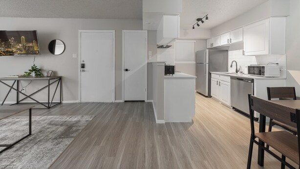 Une cuisine moderne avec des meubles blancs, un coin repas doté d’une table et de chaises en bois, et un tapis gris sur le sol.