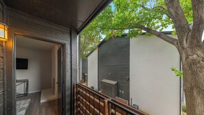 Eine Holztreppe führt zu einem Balkon mit Blick auf ein Gebäude und einen Baum.