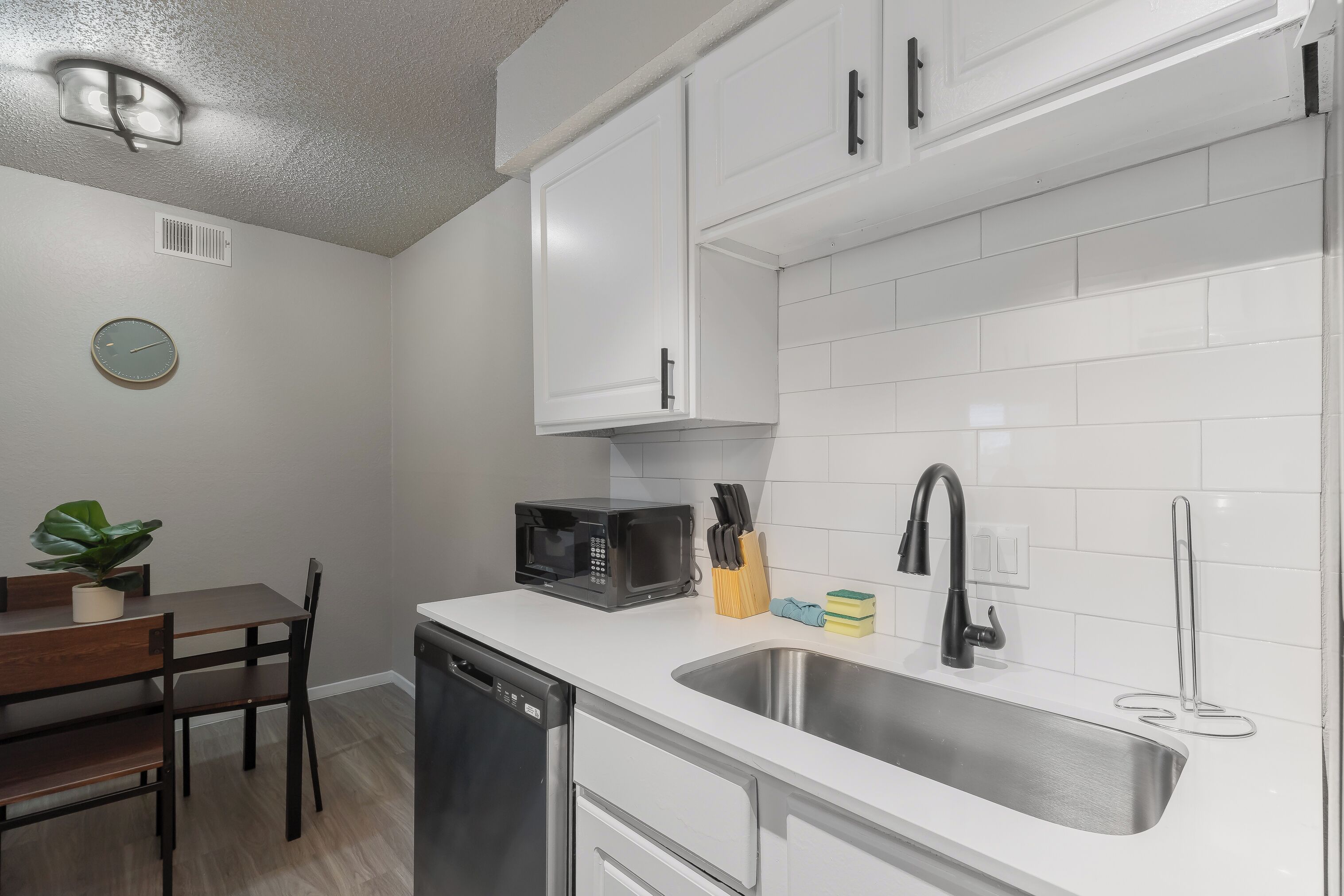 A modern kitchen with white cabinets, a stainless steel sink, a microwave, and a dining area with a table and chairs.