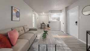 Ein modernes Wohnzimmer mit einer Couch, einem Couchtisch mit Pflanzen und einer Küche im Hintergrund.