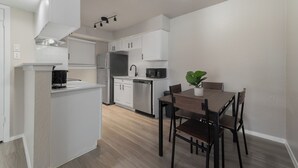 Une cuisine moderne avec des meubles blancs, un four encastré et un coin repas comprenant une table et des chaises en bois.