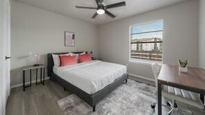 Une chambre à coucher comprenant un lit, un bureau, une chaise, un ventilateur de plafond, une fenêtre et une plante.
