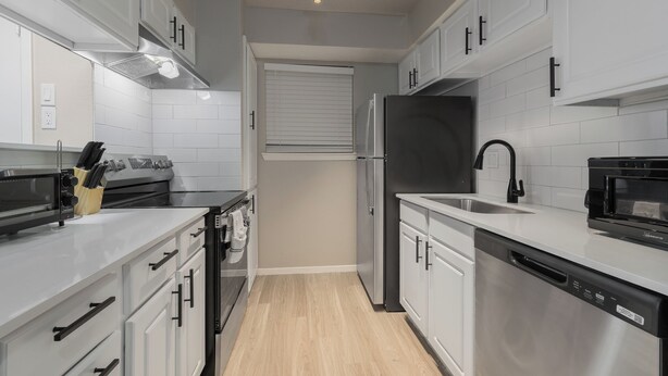 Une cuisine moderne avec des meubles blancs, des appareils électroménagers en acier inoxydable et un plancher en bois.