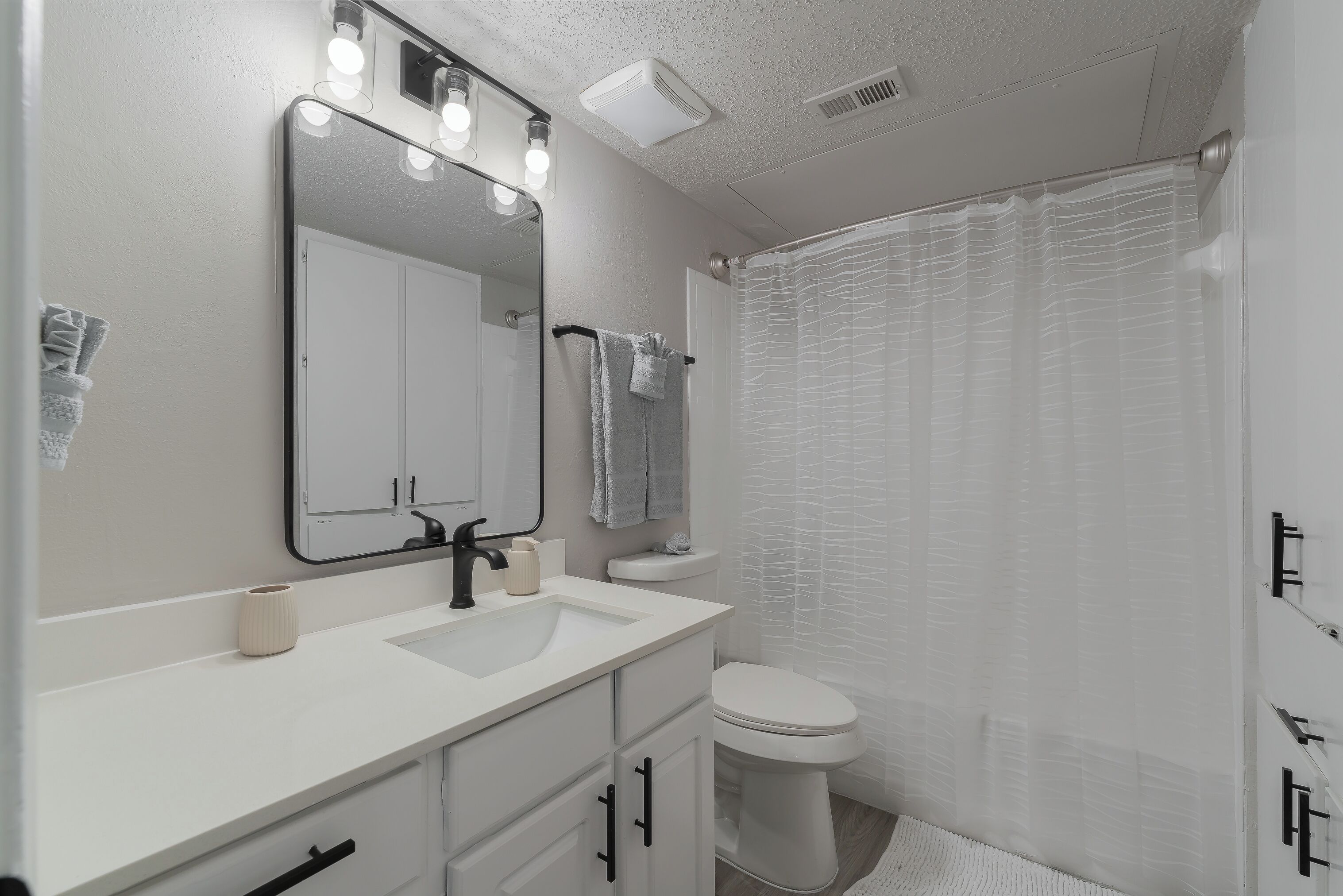 Une salle de bain avec un lavabo blanc, un miroir et des toilettes. On y trouve également un porte-serviettes et un rideau de douche.