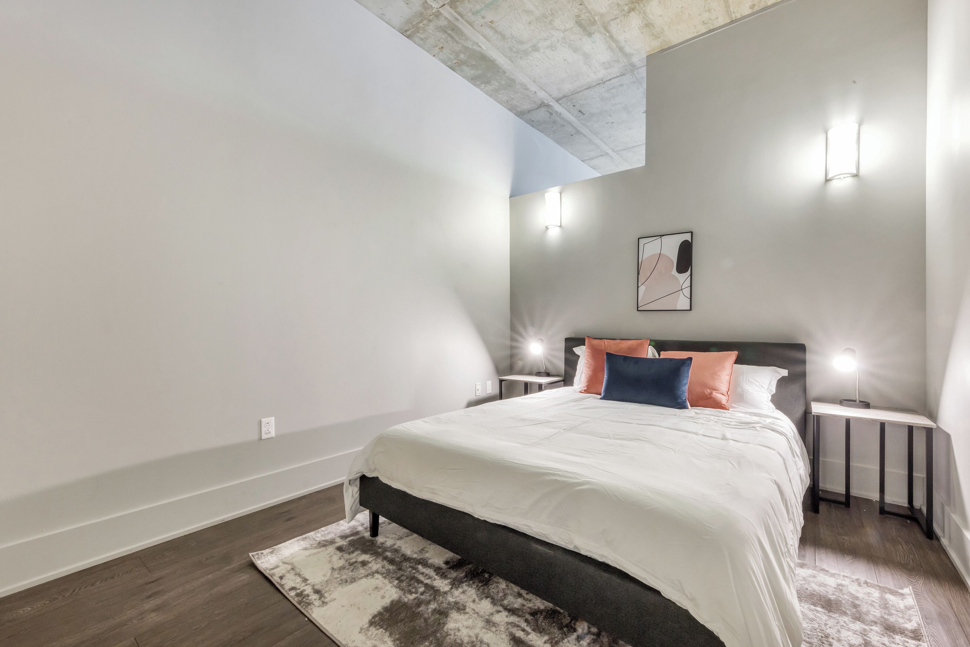 Un dormitorio moderno con una cama grande, dos mesitas de noche e iluminación en la pared.