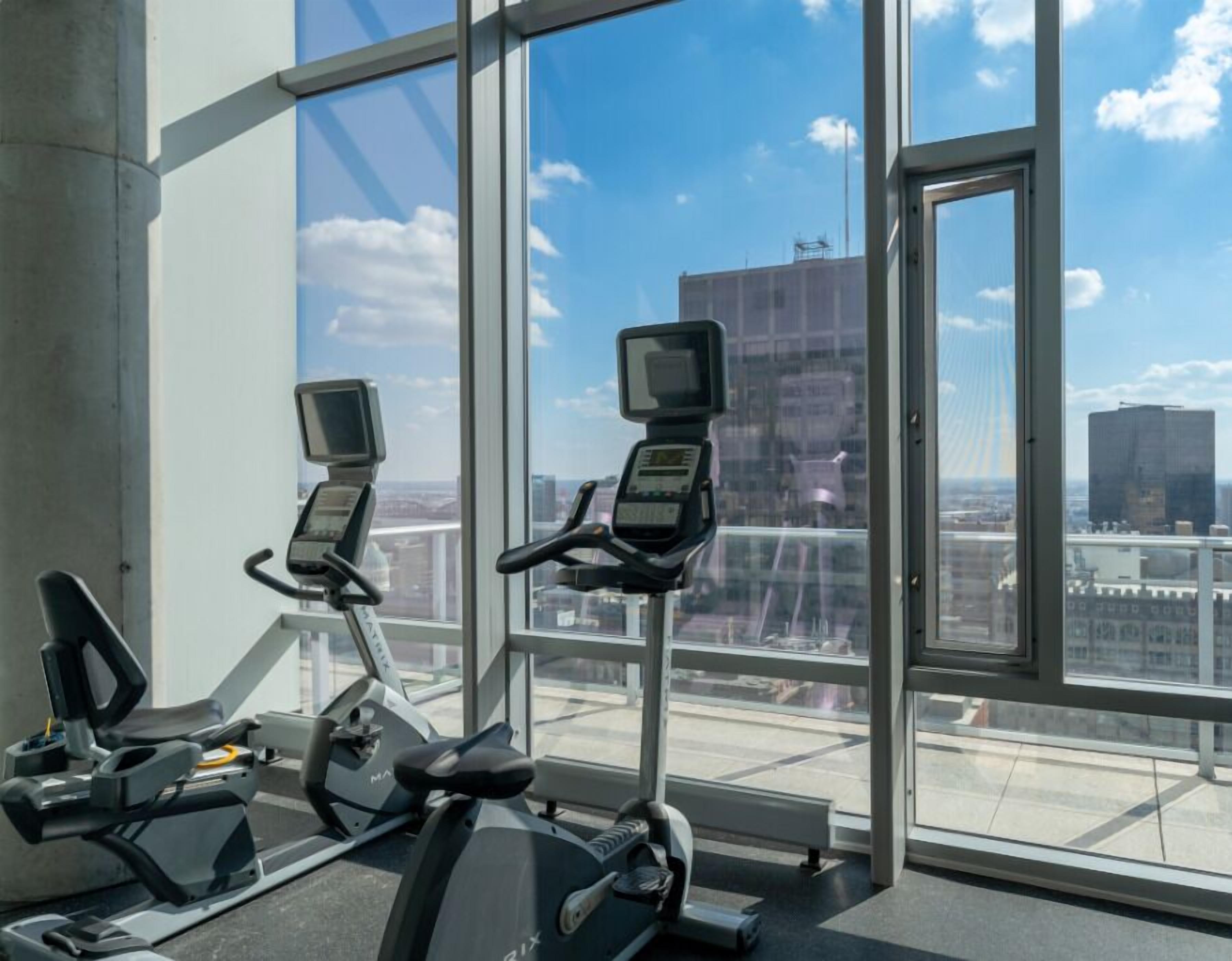 An indoor gym with two stationary bikes and a treadmill, large windows with a city view.