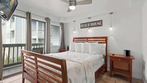 A bedroom with a wooden bed, a ceiling fan, a sign reading "BEACH HOUSE", and a balcony with a view of buildings. - Myrtle Beach Resort 6211 (Myrtle Beach)