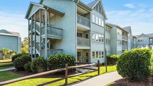 A multi-story residential building with a balcony on each floor, a front porch, and a wooden fence in the front yard. - Myrtle Beach Resort 6211 (Myrtle Beach)