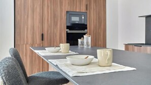Una cocina moderna con armarios de madera, horno empotrado y comedor con una mesa larga dispuesta con cuencos y tazas.
