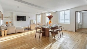 Un salón amplio con suelo de madera, una zona de comedor con mesa de cristal y un sofá.