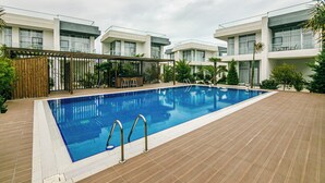 Una piscina rettangolare con scalette in metallo, circondata da un solarium in legno e moderni edifici con balconi.