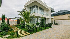 Una moderna casa a due piani con un balcone, circondata da giardini curati e un vialetto lastricato.