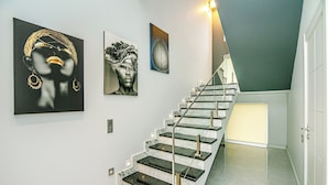 Una moderna scala con gradini in marmo e ringhiere in vetro, che porta a una piattaforma illuminata da un lampadario.