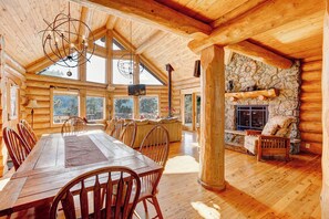 Cozy cabin interior with a stone fireplace, wooden beams, and large window.