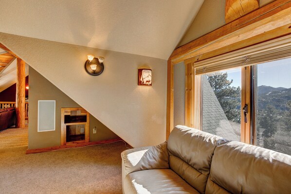 Una sala de estar acogedora con techo inclinado, vigas de madera, un sofá de cuero y un ventanal con vistas al exterior.