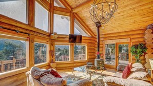 A log cabin interior with large windows, a fireplace, and a cozy seating area.