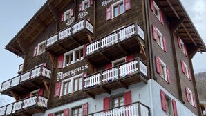 Een hotel met meerdere verdiepingen, balkons, rode luiken en een stenen gevel.