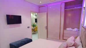 A modern bedroom with a large bed, a TV mounted on the wall, and a wardrobe with a mirror. - Aphrodite Apartment (Tangier)