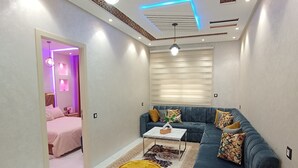 A modern living room with a blue sofa, a coffee table, and a dining area with a marble table. - Aphrodite Apartment (Tangier)