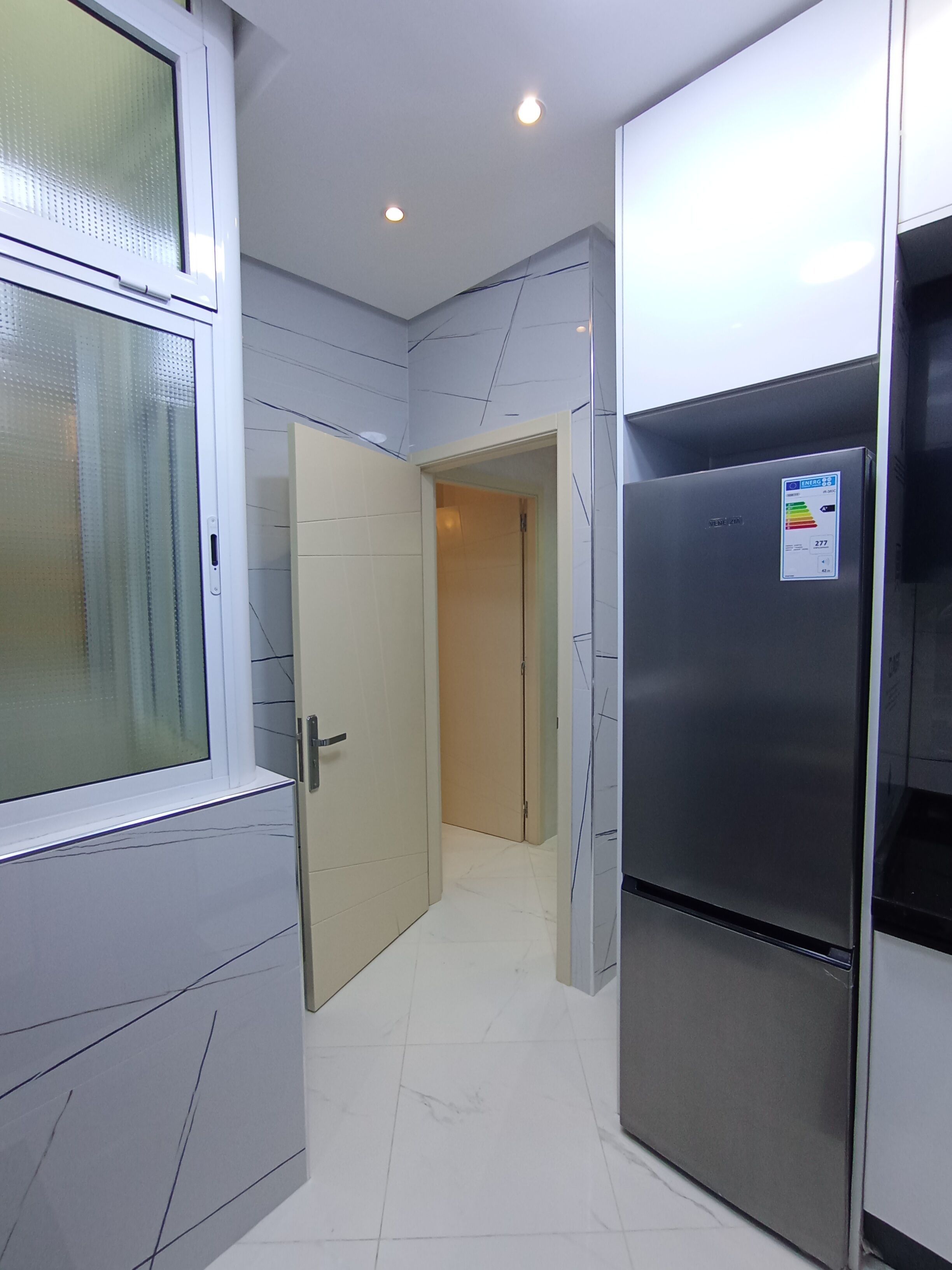 Un pasillo estrecho con una cocina moderna que incluye un refrigerador de acero inoxidable y armarios.
