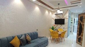 A modern living room with a blue sofa, a white coffee table, and a dining area with yellow chairs. - Aphrodite Apartment (Tangier)