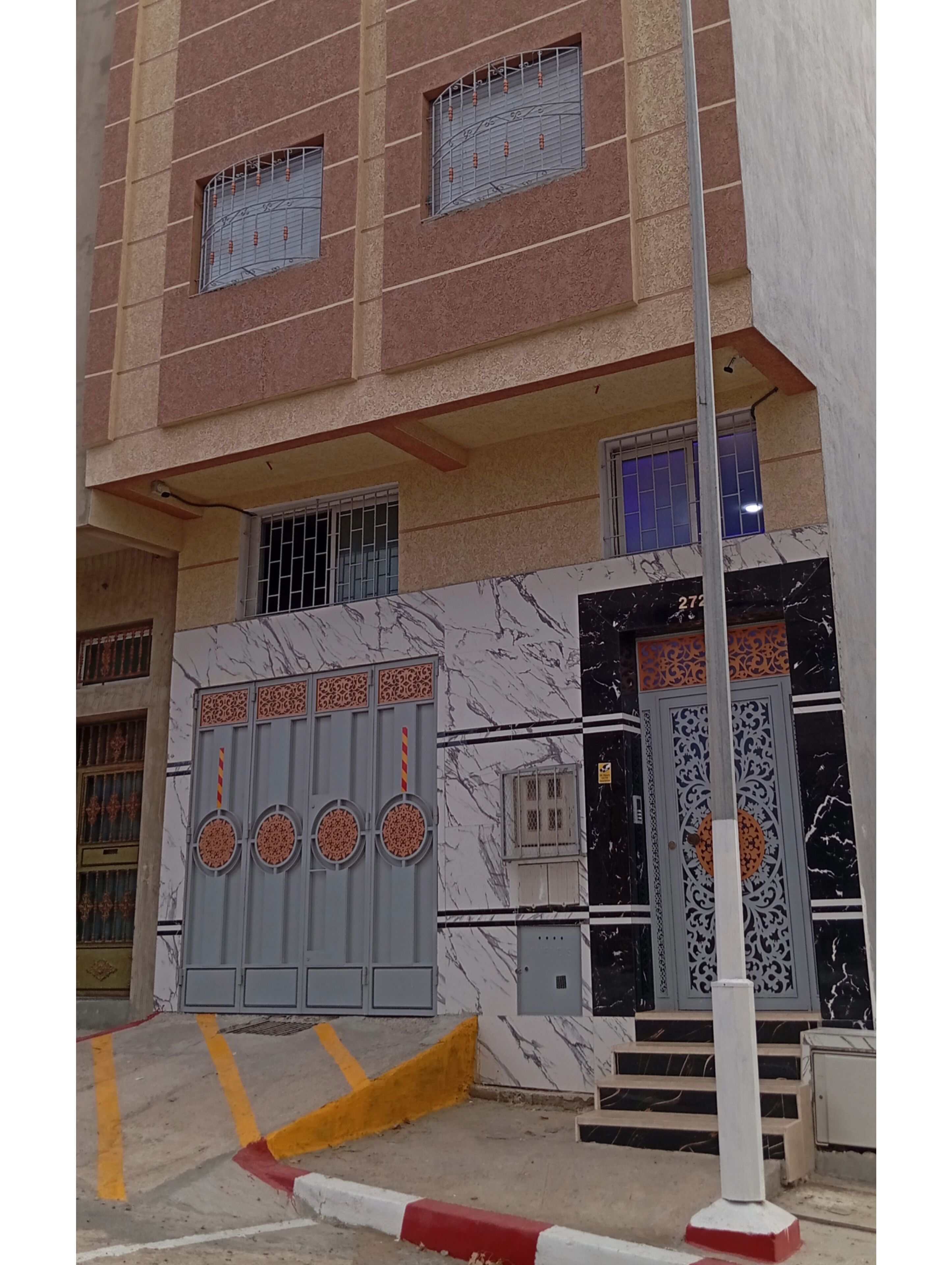 A building with a marble facade, a gated entrance, and a visible number '272' on the door.